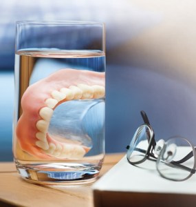 Image of dentures in a glass of water by a bed